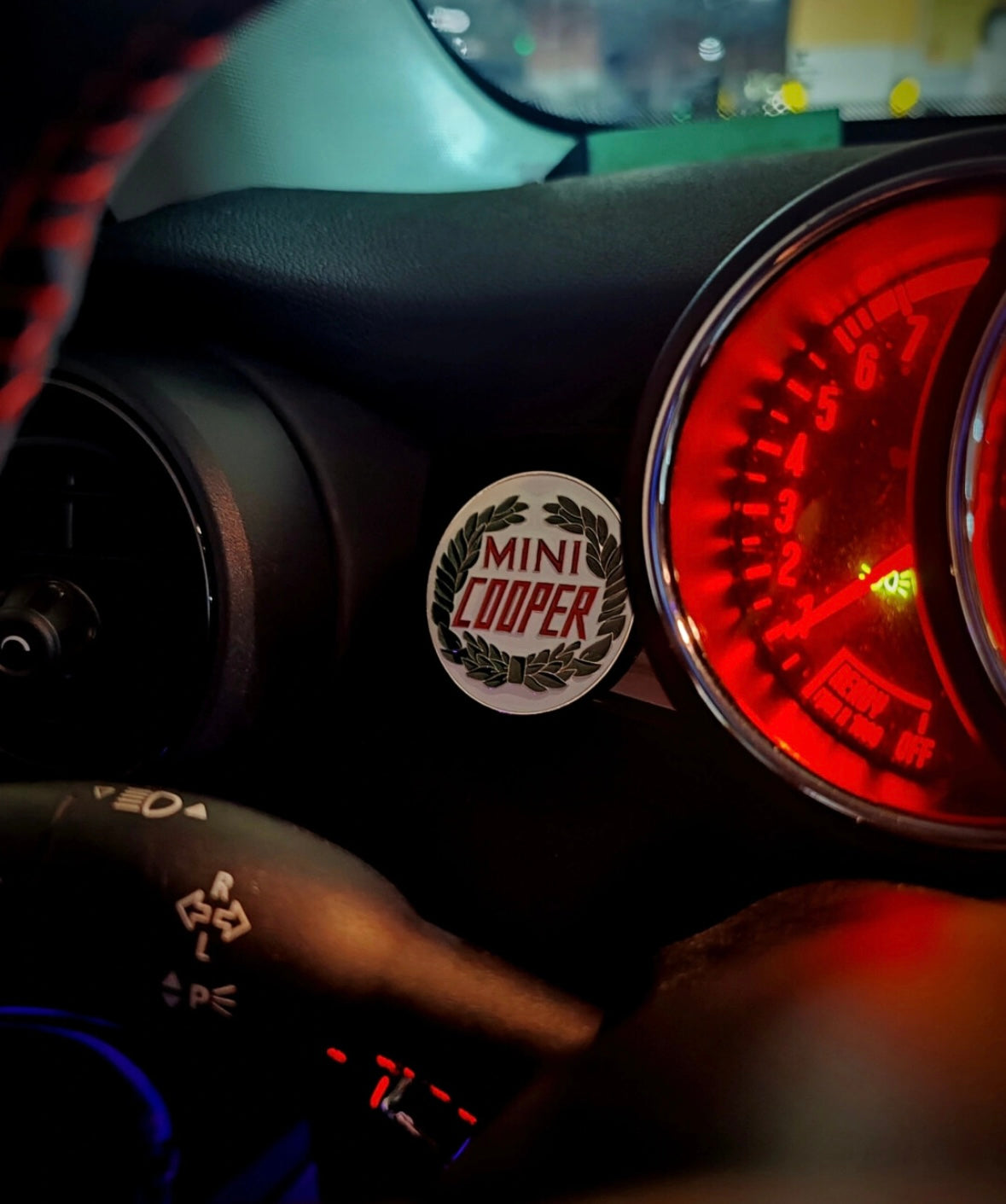 Laurel wreath enamel badge placed next to the dashboard of a MINI Cooper, adding a vintage motorsport touch.
