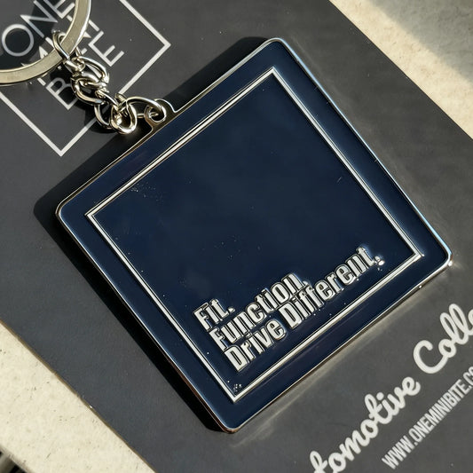 Close-up of ONEMINIBITE logo keychain showing metallic body and glossy enamel finish