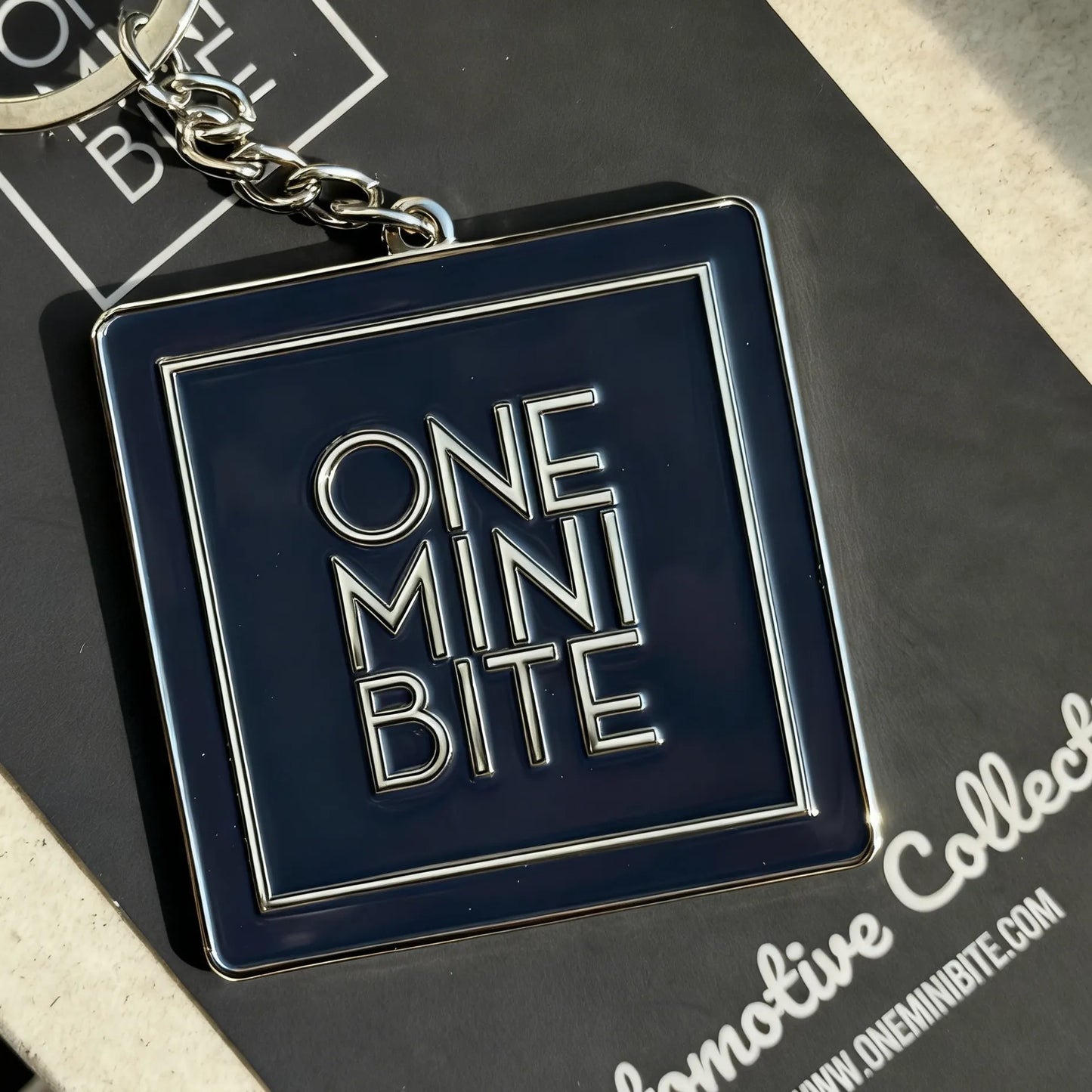 ONEMINIBITE square logo keychain shown in a lifestyle setting attached to keys