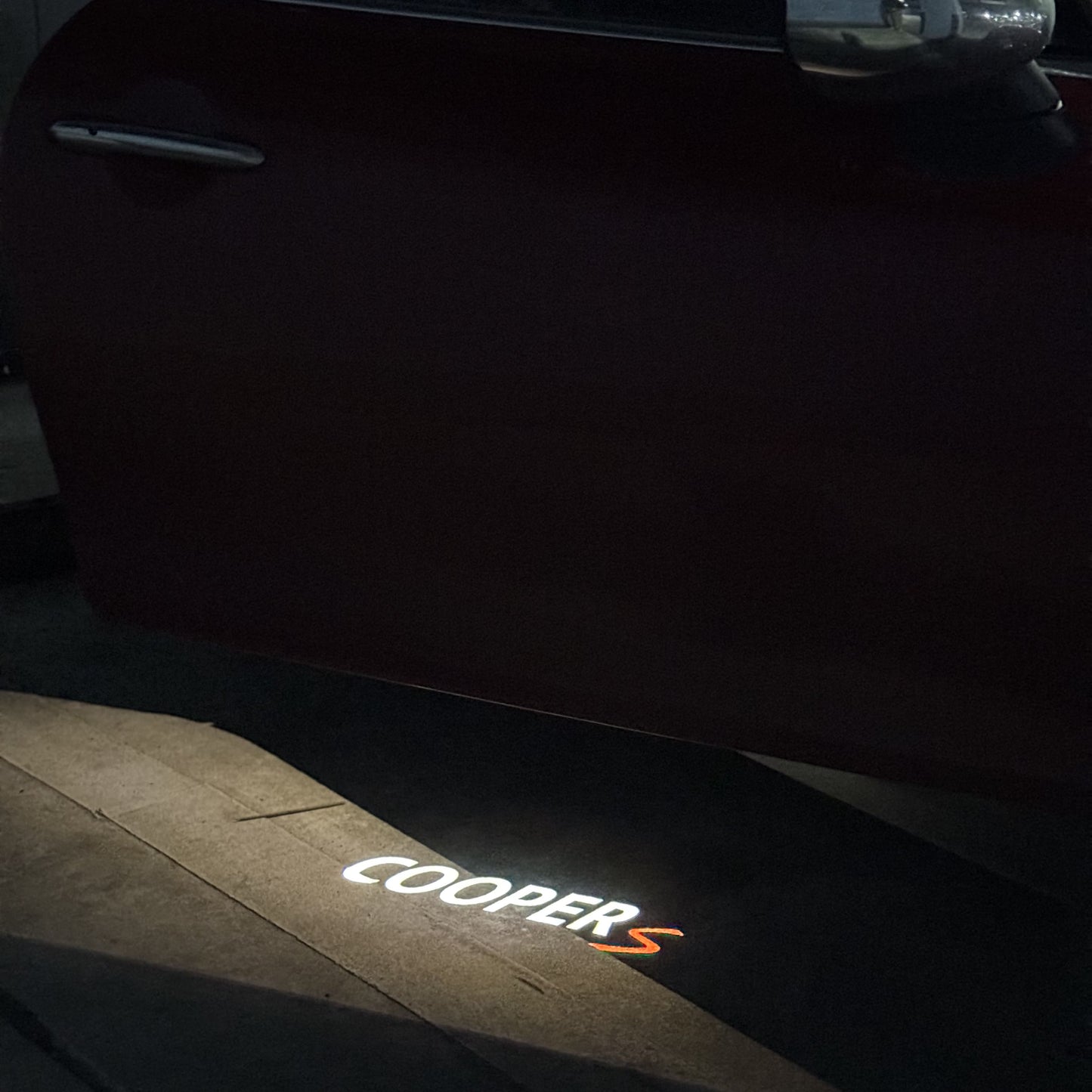 Red Cooper S door logo projection on urban sidewalk from MINI F55 5-door