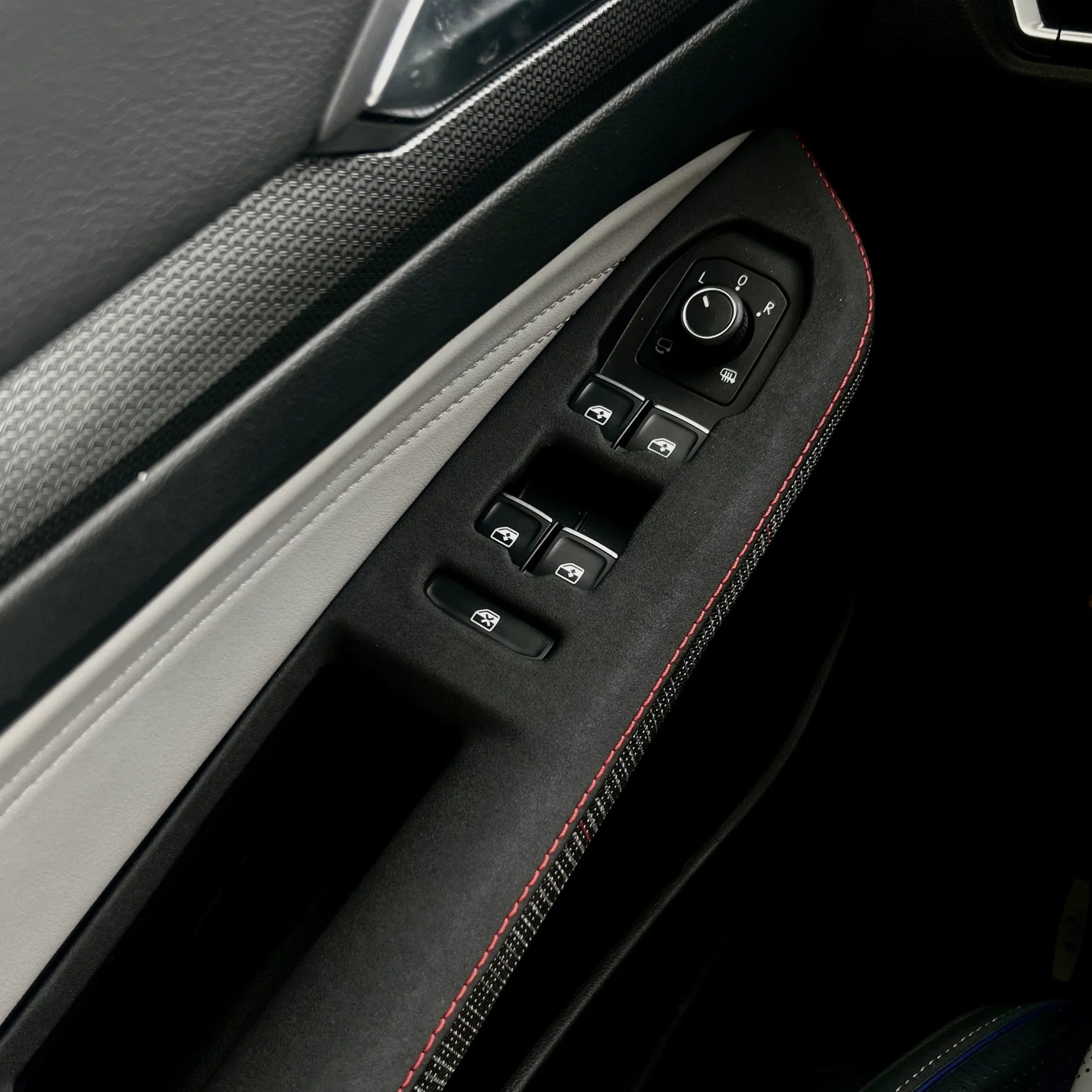 Close-up of the plaid semi-rough leather texture used on the VW Golf Mk8 GTI door control panel cover, showing durable material finish and precision-cut control openings.