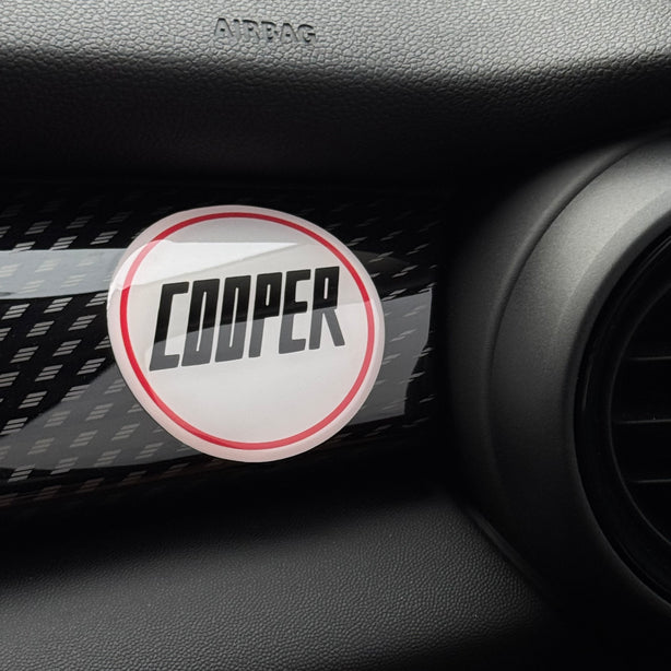 Vintage 'COOPER' gel sticker applied to the passenger side dashboard of a MINI Cooper, adding retro charm to the interior.