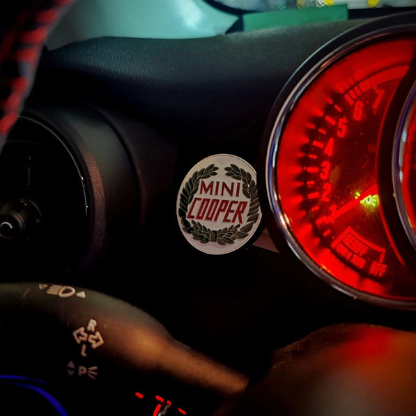 Laurel wreath enamel badge placed next to the dashboard of a MINI Cooper, adding a vintage motorsport touch.