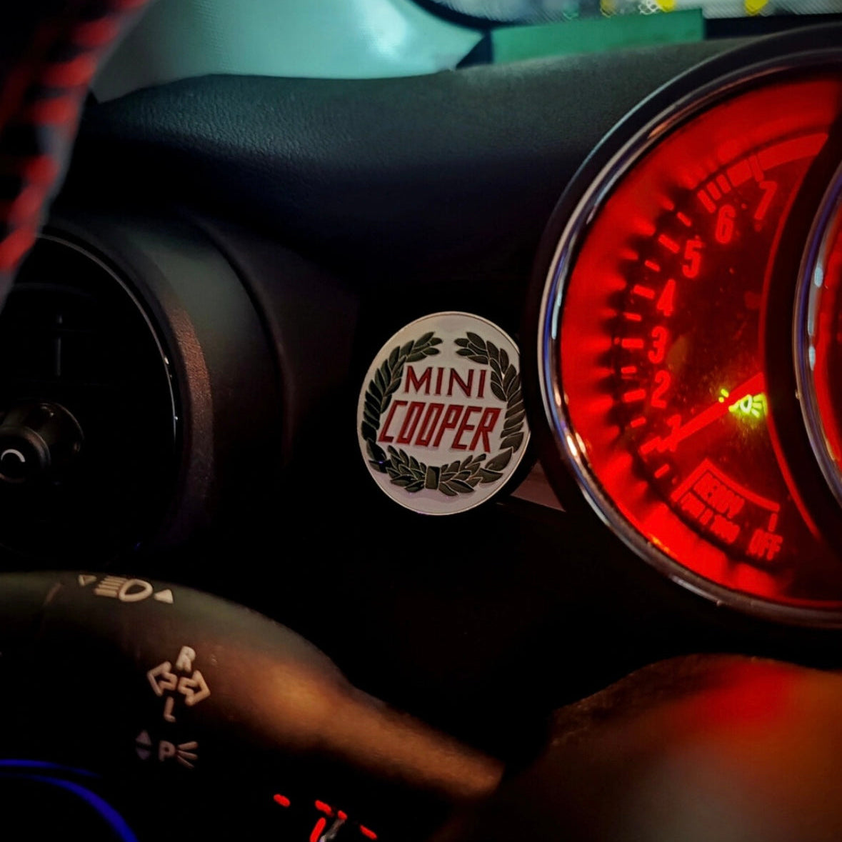 Laurel wreath enamel badge placed next to the dashboard of a MINI Cooper, adding a vintage motorsport touch.