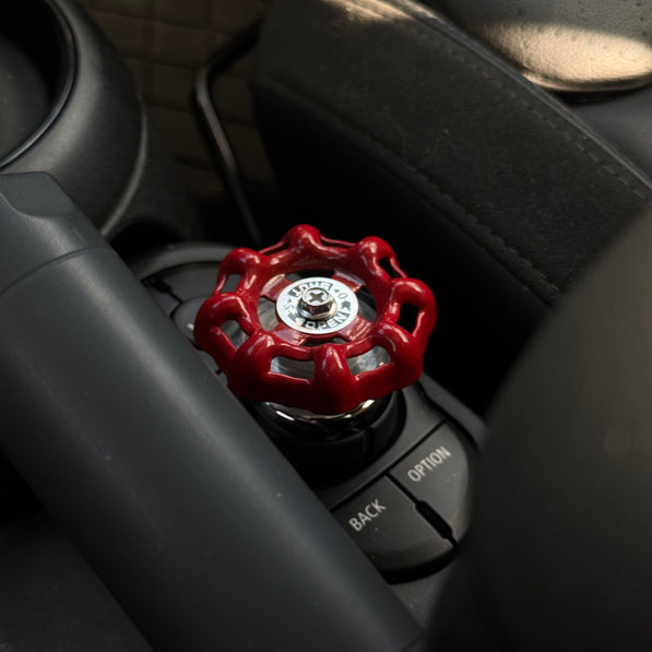 Aluminum red valve-style iDrive button decoration installed on a MINI Cooper F-Series controller, adding a playful touch to the interior.