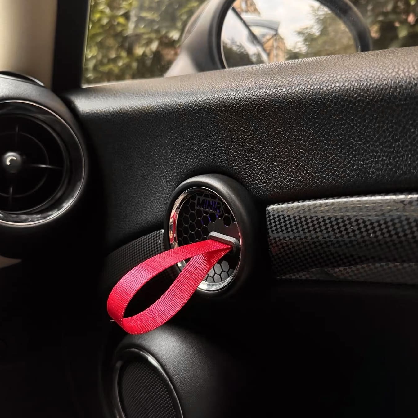 Close-up of red RS-style door pull strap installed on MINI Cooper R56 door panel.