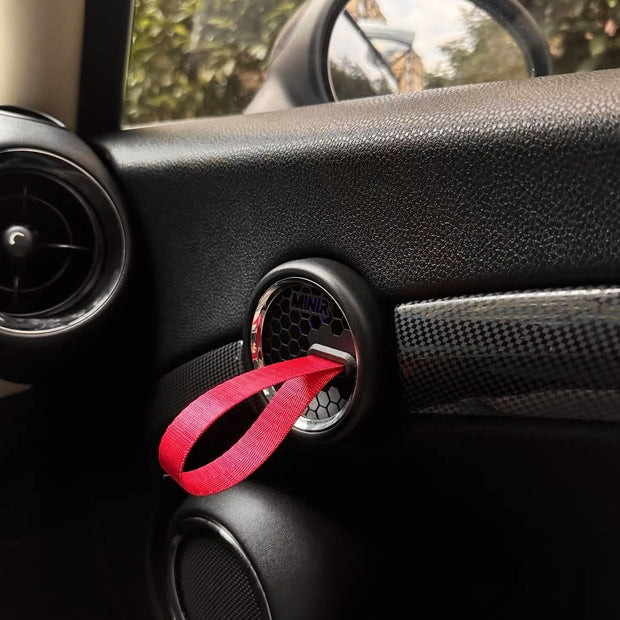 Close-up of red RS-style door pull strap installed on MINI Cooper R56 door panel.