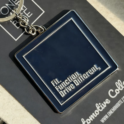 Close-up of ONEMINIBITE logo keychain showing metallic body and glossy enamel finish