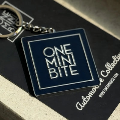 Official ONEMINIBITE square logo keyring with metallic baked-enamel finish, front view