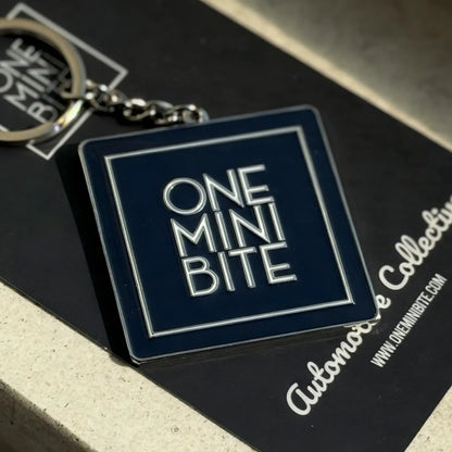 Official ONEMINIBITE square logo keyring with metallic baked-enamel finish, front view