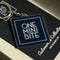 Official ONEMINIBITE square logo keyring with metallic baked-enamel finish, front view